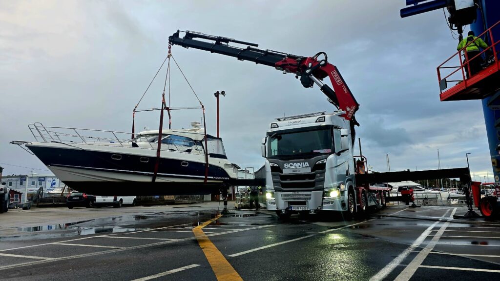 Wilgos bodbil med utfälld kran lyfter en motorbåt vid en hamn.