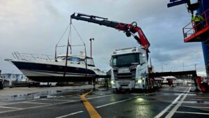 Wilgos bodbil med utfälld kran lyfter en motorbåt vid en hamn.
