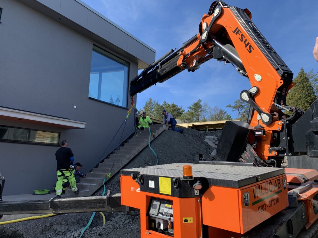 Jekko JF545 från Wilgo vid montage av en betongtrappa intill en husfasad, med flera personer som hjälper till på plats.